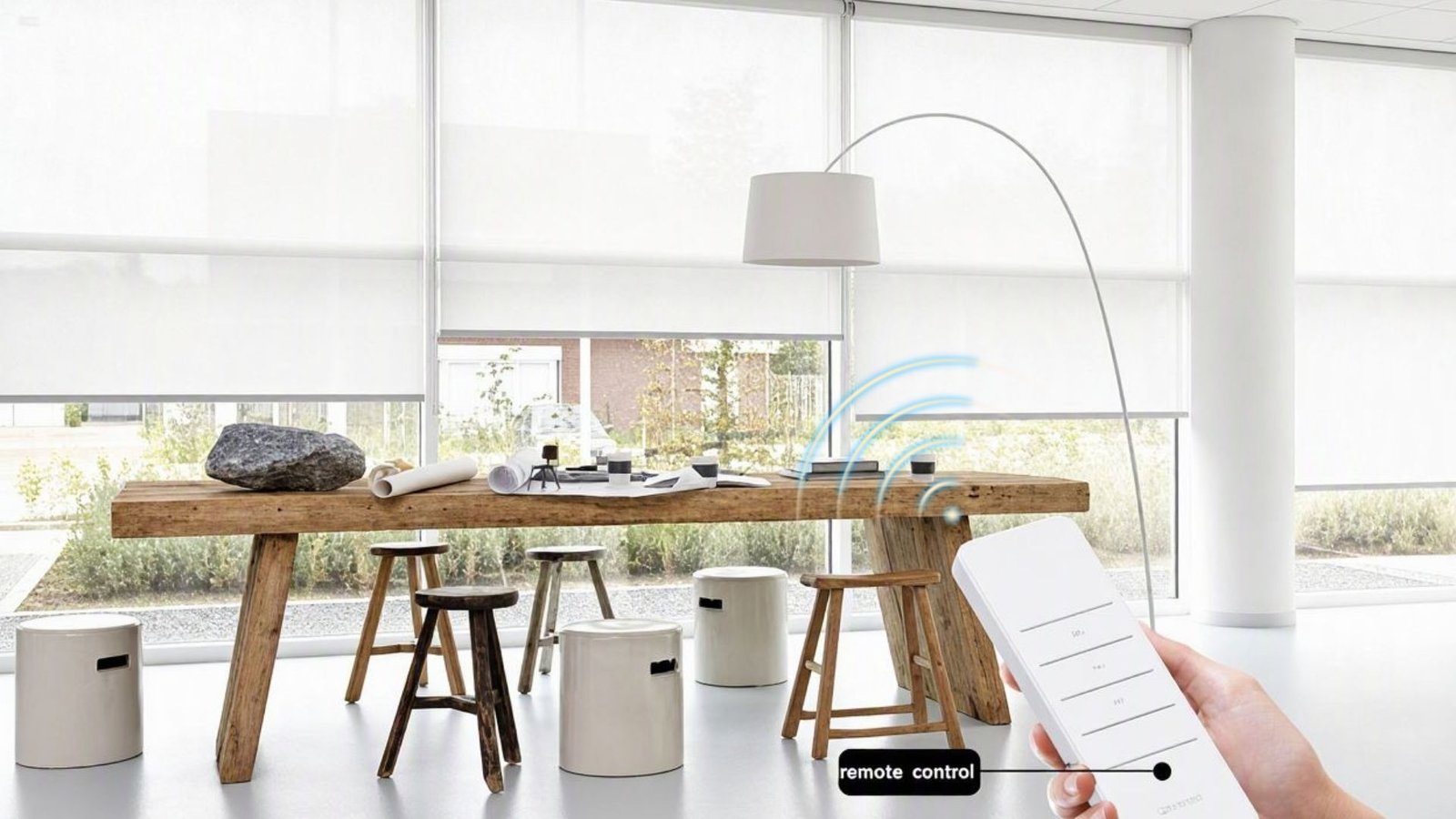 Jual Gorden Elektrik / Gorden Motorized / Electric Blind 1 Roller blind elektrik putih pada jendela besar area kerja dengan remote control di tangan
