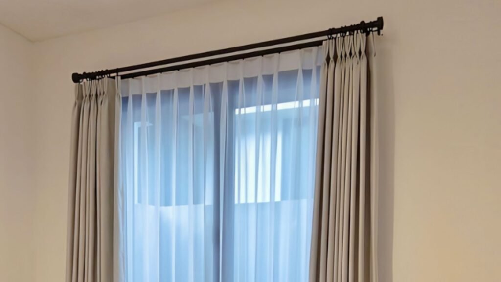 Rel gorden hitam doff batang bulat dengan gorden lipit abu-abu dan vitrase putih pada jendela kamar minimalis